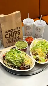 A short, fast-paced promotional video showcasing a lunch spread from Chipotle, featuring burrito bowls, chips, guacamole, salsa, and fruit-based drinks.