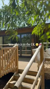 A serene, inviting shot of a waterside lodge at Fairwood Lakes, framed through foreground foliage to create a sense of privacy and natural beauty. The image effectively communicates a peaceful, luxury staycation experience.
