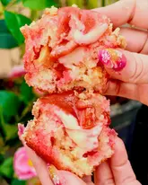 A close-up, appetizing shot of a homemade rhubarb and white chocolate custard crumble muffin being pulled apart to reveal the creamy filling and texture.