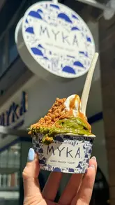 A short, energetic video showcasing the opening of Myka, a new Greek frozen yogurt shop in London. The video features close-up shots of the yogurt being dispensed, a variety of toppings being added, and the aesthetic interior of the venue.