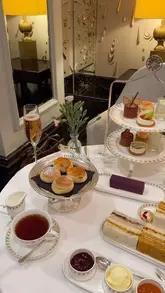 A high-quality, top-down shot of an elegant afternoon tea spread, featuring scones, sandwiches, pastries, and champagne, set in a luxurious hotel environment.
