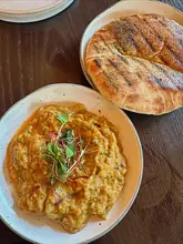A clean, overhead shot of a lunch spread at Brother Marcus, featuring a bowl of smoky aubergine baba ghanoush topped with microgreens and a side of grilled pita bread on a dark wooden table.