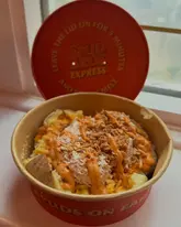 A close-up shot of a loaded jacket potato from Spud Bros Express, featuring toppings like tuna mayo, cheese, and crispy onions, served in a branded takeaway container.