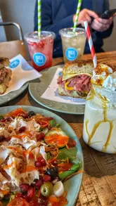 A short vlog-style video showcasing a local deli called Deli H, highlighting their fresh focaccia sandwiches, salads, and drinks.