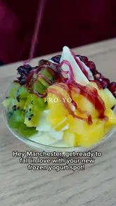 A close-up shot of a bowl of frozen yogurt topped with fresh kiwi, pineapple, and a berry drizzle, promoting a new frozen yogurt spot in Manchester.