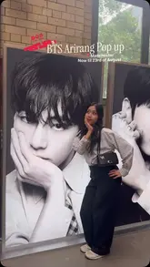 A photo of a visitor posing in front of large promotional posters at the BTS Arirang pop-up event in Manchester.