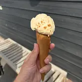 A simple, casual, eye-level shot of a single scoop of ice cream in a cone, held against a grey wooden wall.