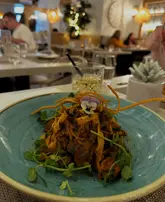A close-up shot of a lamb ragu tagliatelle dish served on a blue plate, captured in a dimly lit, atmospheric restaurant setting.