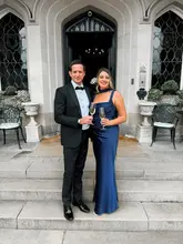A couple dressed in formal evening wear poses for a photo in front of the entrance to Dundas Castle, holding glasses of champagne.