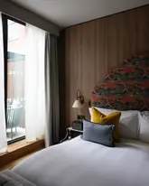 A professional, high-quality interior shot of a hotel room at The Imperial Bloomsbury, highlighting the bed, the unique headboard design, and the natural light from the window.