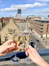 A bright, high-quality shot of two people toasting with glasses of sparkling wine against a clear, sunny backdrop of the Liverpool skyline, specifically featuring the Metropolitan Cathedral.