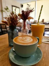 A casual, cozy shot of a coffee and a juice at a cafe, featuring latte art and dried flower decor.