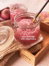 A high-quality, aesthetically pleasing food photography shot of pickled red onions in a glass jar, presented on a rustic wooden tray with burlap. The image is well-lit and styled to look like a professional food blog or recipe post.