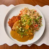 A clean, overhead shot of a homemade chicken katsu curry served with fried rice, garnished with spring onions. The image is bright and well-composed, focusing on the texture of the breaded chicken and the curry sauce.