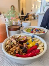 A bright, inviting shot of two smoothie bowls, a coffee, and a juice, likely taken at a cafe during a weekend breakfast or brunch. The focus is on the fresh, colourful ingredients in the foreground bowl, creating an appealing and healthy aesthetic.