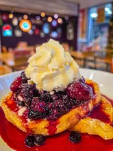 A close-up shot of a French toast stack topped with berry compote, whipped cream, and honey, served at RBF Café.
