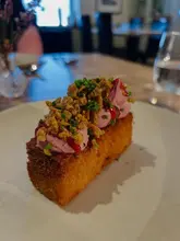 A close-up, high-quality shot of a sophisticated starter dish, featuring a golden-fried base topped with a smooth pink mousse, crispy garnish, and fresh chives, served on a simple white plate.