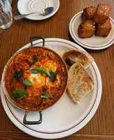 A high-quality, overhead shot of a brunch meal featuring Italian baked eggs in a copper pan and a side of crispy hash browns, set on a wooden table.