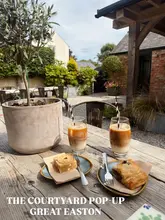 A bright, inviting outdoor shot of a cafe table set with iced coffees and pastries, capturing a relaxed, sunny atmosphere in a courtyard setting.