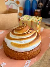 A close-up shot of a key lime pie meringue cookie with a funfetti cake slice in the background, presented on branded paper.