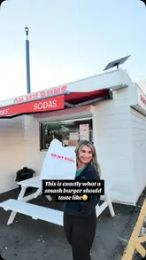 A creator visits a burger takeaway spot called Oh My Buns, showcasing the menu, the smash burgers, fries, milkshakes, and cookies, and provides a positive review while eating in her car.