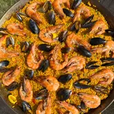 A vibrant, overhead shot of a homemade seafood paella served in a traditional pan, featuring well-cooked rice, large prawns, and mussels.