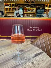 A straightforward, eye-level shot of a glass of sparkling rosé wine placed on a wooden table, with the interior of a wine bar visible in the background.