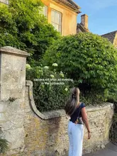 A lifestyle shot capturing a moment from an evening in the Cotswolds, featuring a person standing in front of a stone wall and greenery, likely at a hotel or inn.