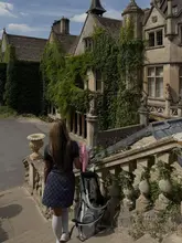A high-quality, aesthetic shot of a visitor walking up the stone steps towards a historic, ivy-clad manor house in the Cotswolds, carrying a golf bag. The image captures a serene, 'old money' countryside atmosphere, emphasizing the luxury and leisure aspects of the venue.