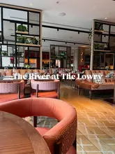 A wide-angle interior shot of The River Restaurant at The Lowry Hotel, showcasing the warm, ambient lighting and comfortable, sophisticated seating arrangement of the dining room.