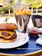 A close-up, eye-level shot of a double cheeseburger and a metal cone of fries served on a blue table, likely at an outdoor venue.