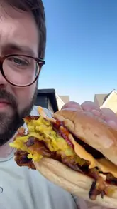 A home cooking video where the creator demonstrates how to make an onion bhaji smash burger on a BBQ grill, inspired by a poor experience with a local Indian takeaway.