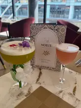 A promotional shot featuring two signature cocktails alongside a menu at Noel's Bar & Restaurant, highlighting the venue's aesthetic and drink presentation.