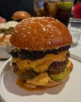 A close-up, eye-level shot of a stacked burger in a restaurant setting, focusing on the texture of the bun and the layers of the patty and cheese.