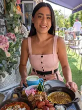 A bright, inviting photo of a woman enjoying a Turkish brunch spread at an outdoor table, effectively showcasing the restaurant's food and atmosphere.