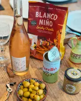 A high-quality, well-lit flat lay of a 'picky bits' spread featuring tortilla chips, olives, mustard, and wine, captured in a casual home setting.