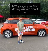 A promotional image for a 'Young Driver' experience, featuring a young boy standing in front of an orange training car in a car park. The image uses a text overlay to frame the content as a 'POV' style video/photo.