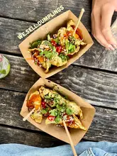 An overhead, natural-light shot of two cardboard trays of dumplings topped with fresh cilantro and chili, served on a rustic wooden table at an outdoor event.