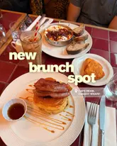 A bright, overhead shot of a brunch spread featuring pancakes with bacon, Turkish eggs, hash browns, and an iced coffee, set on a distinctive red tiled table.