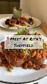 A review of a cafe called 'Meet at Rita's' in Oughtibridge, Sheffield, highlighting their extensive vegan and vegetarian menu options, including campfire beans and pancake stacks, as well as the cafe's atmosphere and outdoor seating.