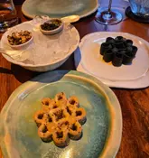 A high-quality, top-down shot of a fine dining tasting menu course at a Michelin-starred Thai restaurant. The image features intricate, flower-shaped crackers served with caviar and other accompaniments, presented on artisanal ceramic plates.