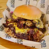 A close-up, high-angle shot of a loaded smash-style burger served in a branded paper-lined basket, highlighting the indulgent and messy nature of the food.