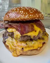 A high-quality, close-up shot of a double bacon cheeseburger, highlighting the melted cheese, crispy bacon, and toasted bun. The image is well-lit and focuses on the appetizing textures of the food.