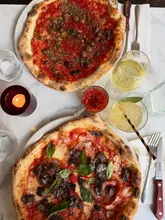A high-quality, overhead flat-lay shot of two pizzas served on a marble table, accompanied by drinks and a candle, capturing a classic casual dining experience.