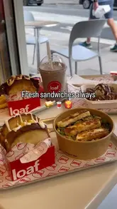 A short, energetic review of a sandwich shop called Loaf, featuring close-ups of their smash burger, truffle scrambled egg sandwich, halloumi salad, and French toast sticks.