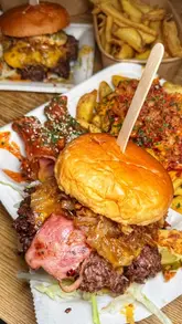 A group of friends visits a burger stall located within a food hall and brewery setting in Leeds, showcasing their meal of smash burgers, loaded fries, and wings alongside pints of beer.