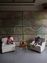 A high-quality, symmetrical shot of two children sitting in armchairs in a stylish hotel lounge, featuring a large map on the wall. The image captures a relaxed, family-friendly atmosphere within a premium hotel setting.