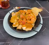 A close-up, top-down shot of a prawn and potato tapas dish served in a small black skillet, captured during a market food crawl.