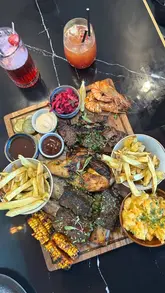 A food review video showcasing a BBQ platter, tacos, and cocktails at Smoky Boys in Milton Keynes. The video features close-up shots of the food, including ribs, grilled prawns, corn, and mac & cheese, as well as a brief look at the menu and venue interior.