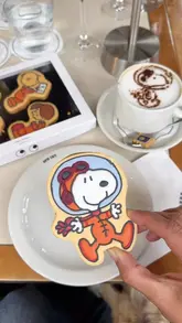 A short, energetic reel showcasing a Snoopy-themed pop-up cafe and shop. The video features close-ups of branded cookies, latte art, and various merchandise, along with a shot of the venue's exterior. It highlights the playful, intergalactic theme of the collaboration.